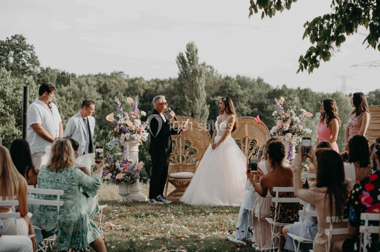 Cérémonie de mariage en plein air avec un officiant s'adressant à la mariée devant des invités assis.