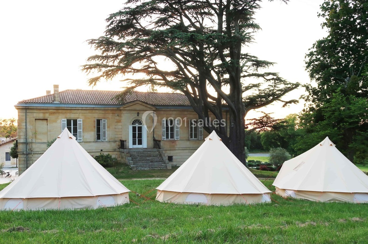 Trois tentes blanches installées sur une pelouse devant une maison ancienne entourée d'arbres au coucher du soleil.