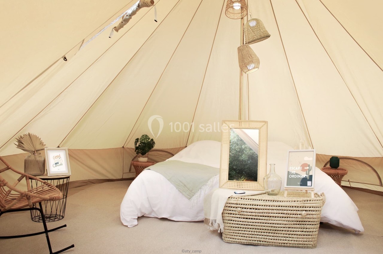 Intérieur d'une tente aménagée avec un lit, des décorations naturelles et un mobilier en osier.