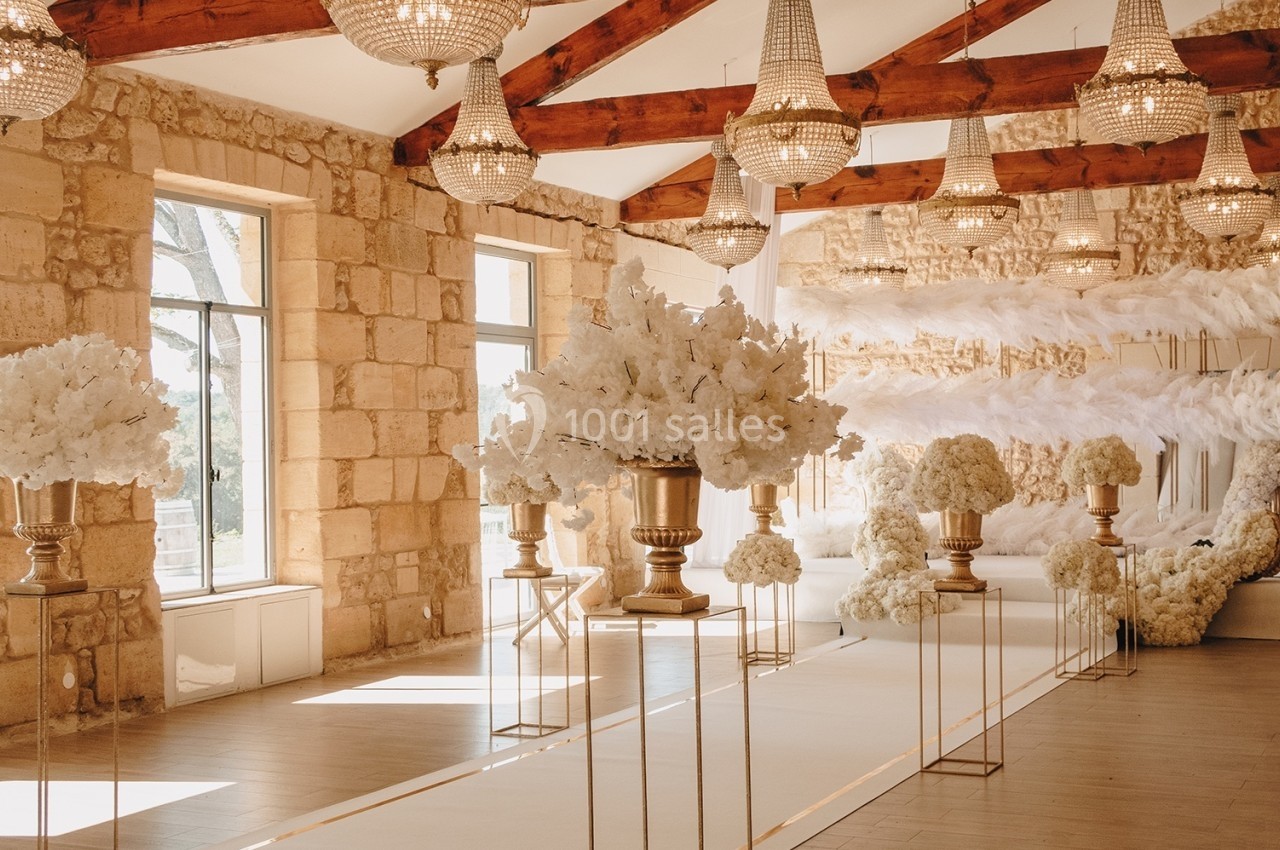 Salle de réception décorée de fleurs blanches, lustres suspendus et murs en pierre apparente.