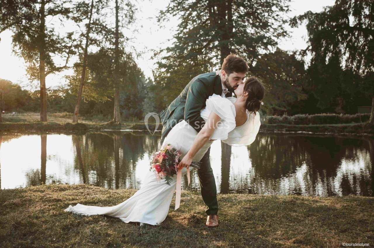 Un couple en tenue de mariage s'embrasse près d'un étang au coucher du soleil.