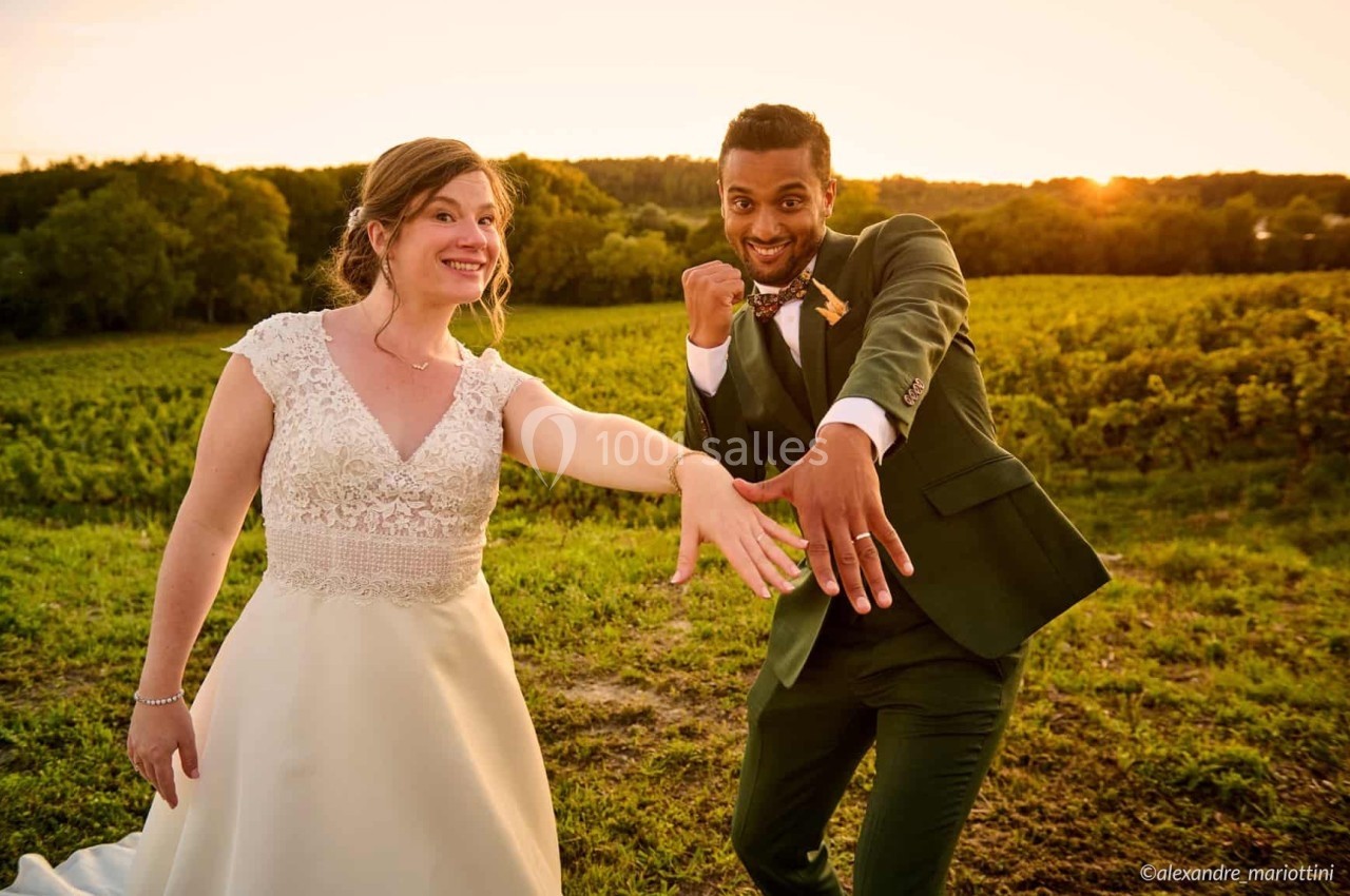 Un couple en tenue de mariage montre leurs alliances dans un champ au coucher du soleil.
