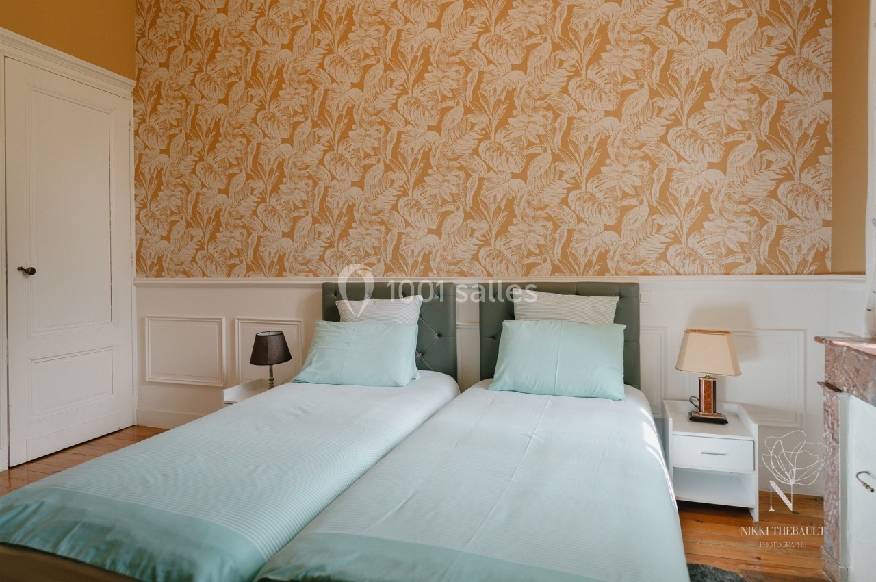 Deux lits simples avec linge de lit vert clair dans une chambre au mur tapissé de motifs floraux jaunes.