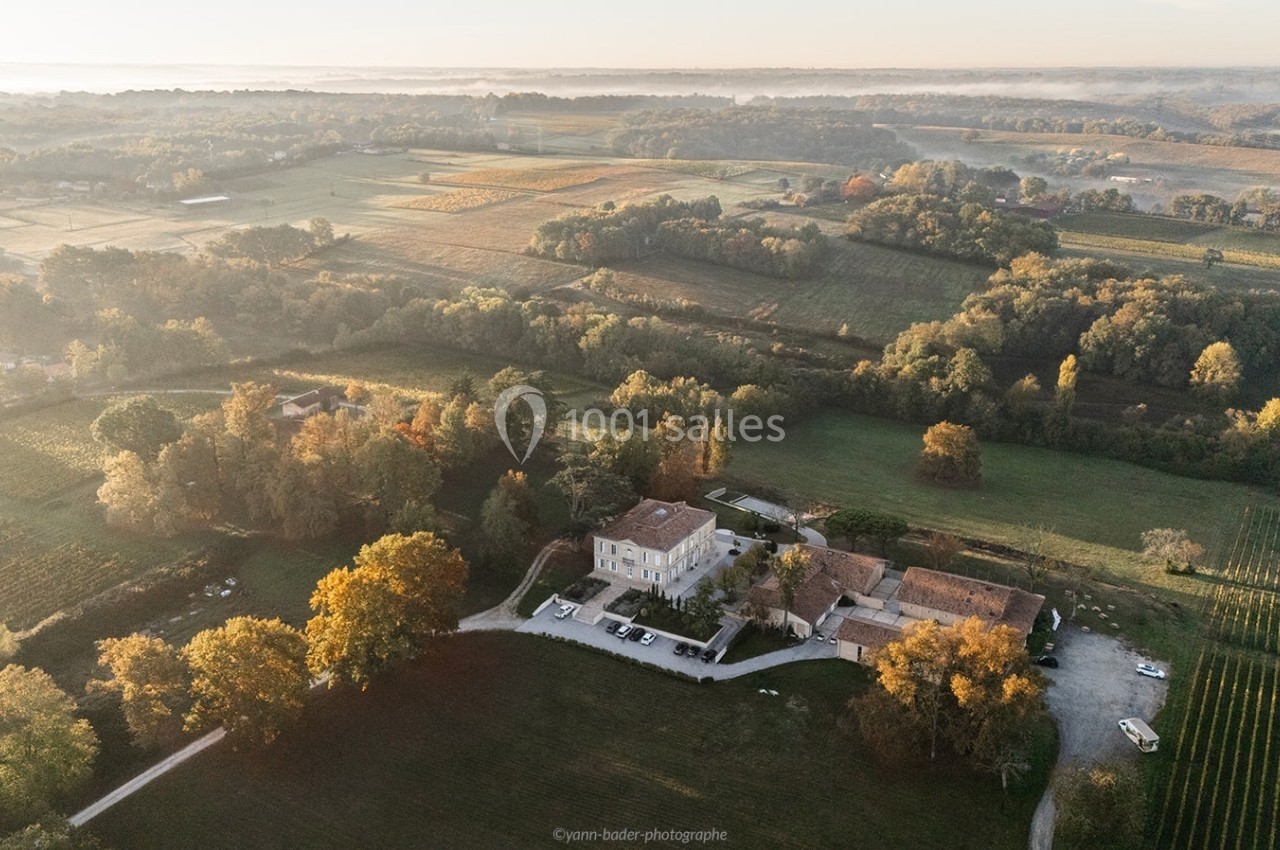Vue aérienne d'une propriété entourée de champs, de vignes et de forêts sous une lumière douce du matin.
