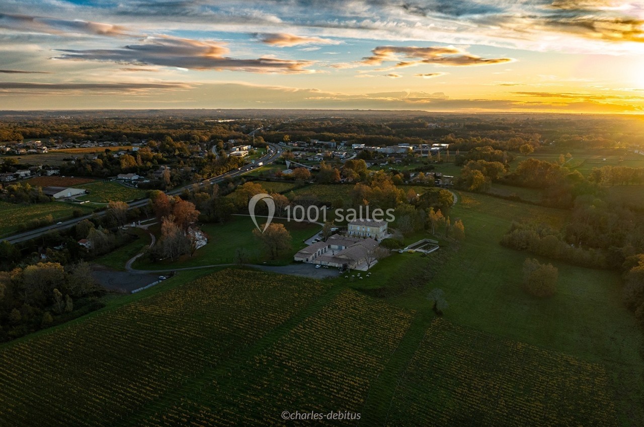 Vue aérienne d'une campagne au coucher du soleil, avec un grand bâtiment entouré de champs et de végétation.