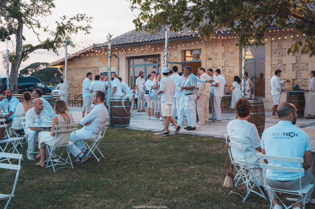 Groupe de personnes en tenue blanche discutant et partageant un moment convivial en extérieur près d'un bâtiment en pierre.