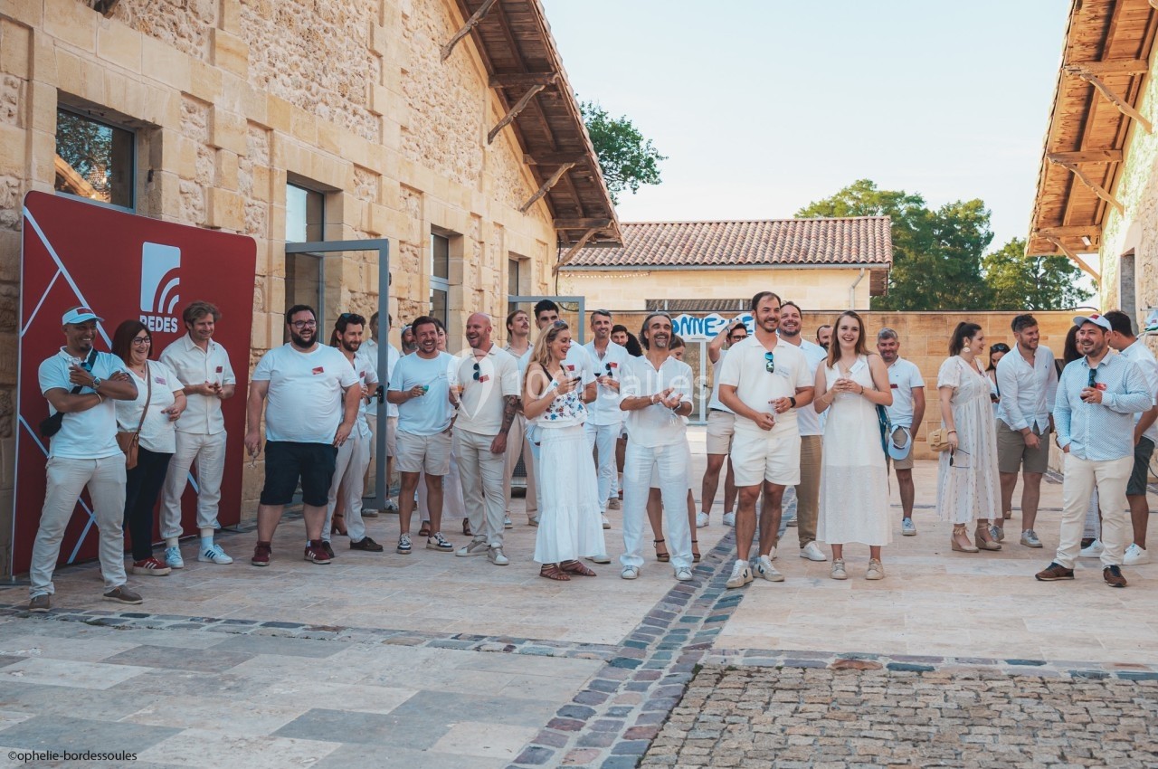 Un groupe de personnes en tenue estivale posant devant un bâtiment en pierre dans une cour ensoleillée.