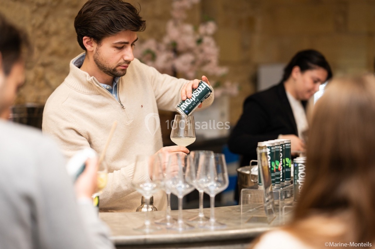 Un homme verse une boisson gazeuse dans un verre sur un comptoir, entouré de plusieurs personnes.