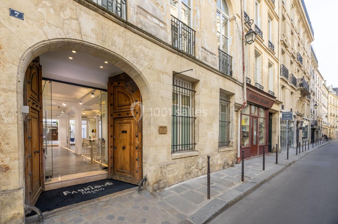 Façade d'un bâtiment en pierre avec une entrée voûtée en bois, donnant sur une rue pavée bordée de boutiques.
