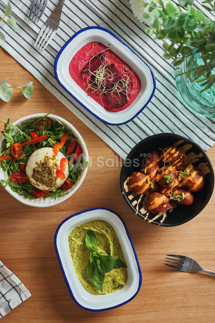 Quatre plats variés sur une table en bois, comprenant salade, houmous, brochettes et tartinade de betterave.