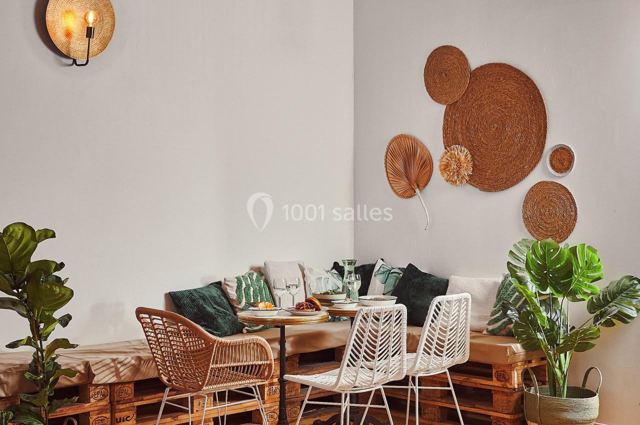 Coin repas cosy avec table en bois, chaises en rotin, coussins verts, plantes et décorations murales en osier.