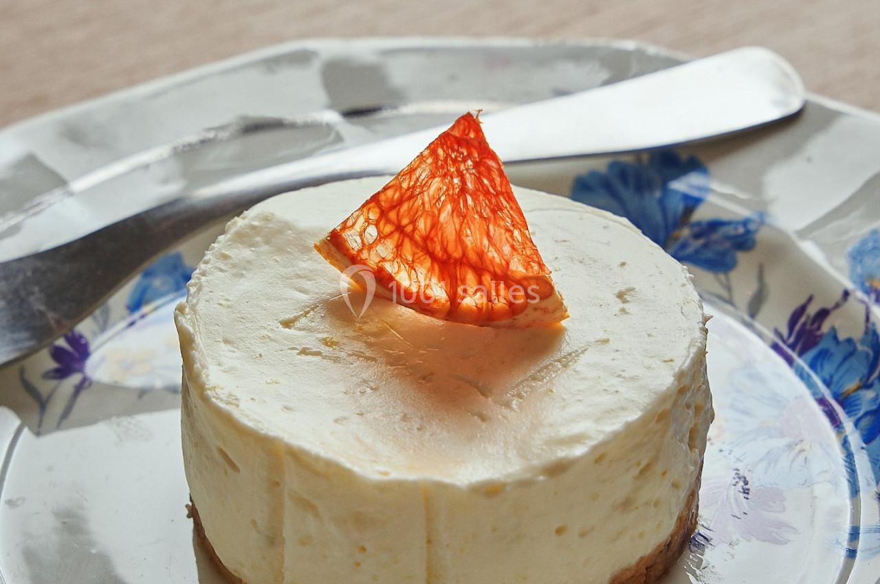 Gâteau au fromage individuel sur une assiette fleurie, décoré d'un segment d'agrume rouge.