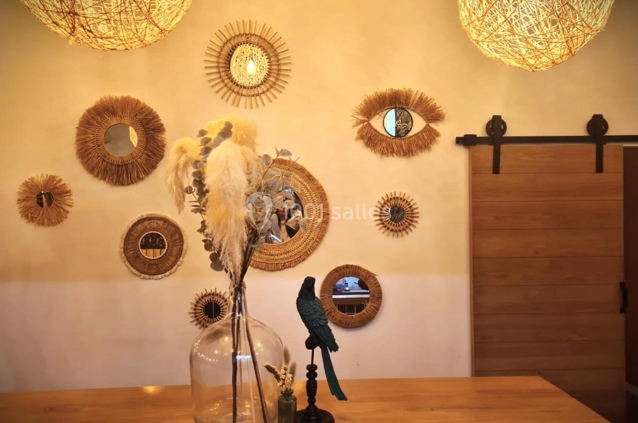 Décoration murale avec miroirs en rotin, vase en verre contenant des fleurs séchées et statue d'oiseau sur une table en bois.
