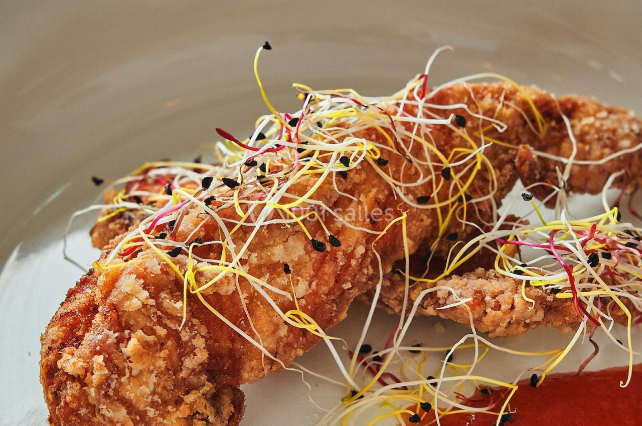 Plat de crevette panée garnie de pousses colorées, accompagné d'une sauce rouge servie dans une assiette blanche.