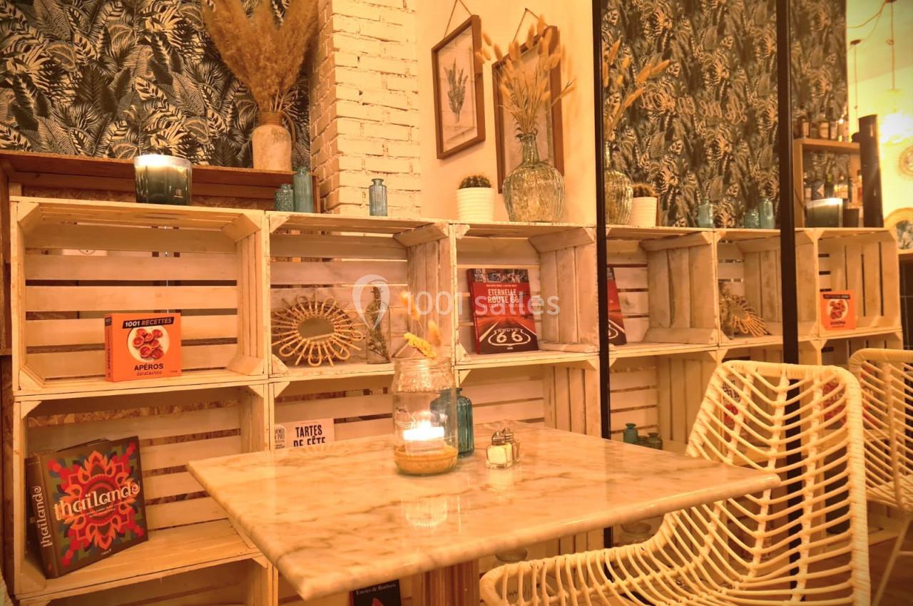 Étagères en bois décorées, table en marbre avec bougie, chaises en rotin, ambiance chaleureuse et végétale.