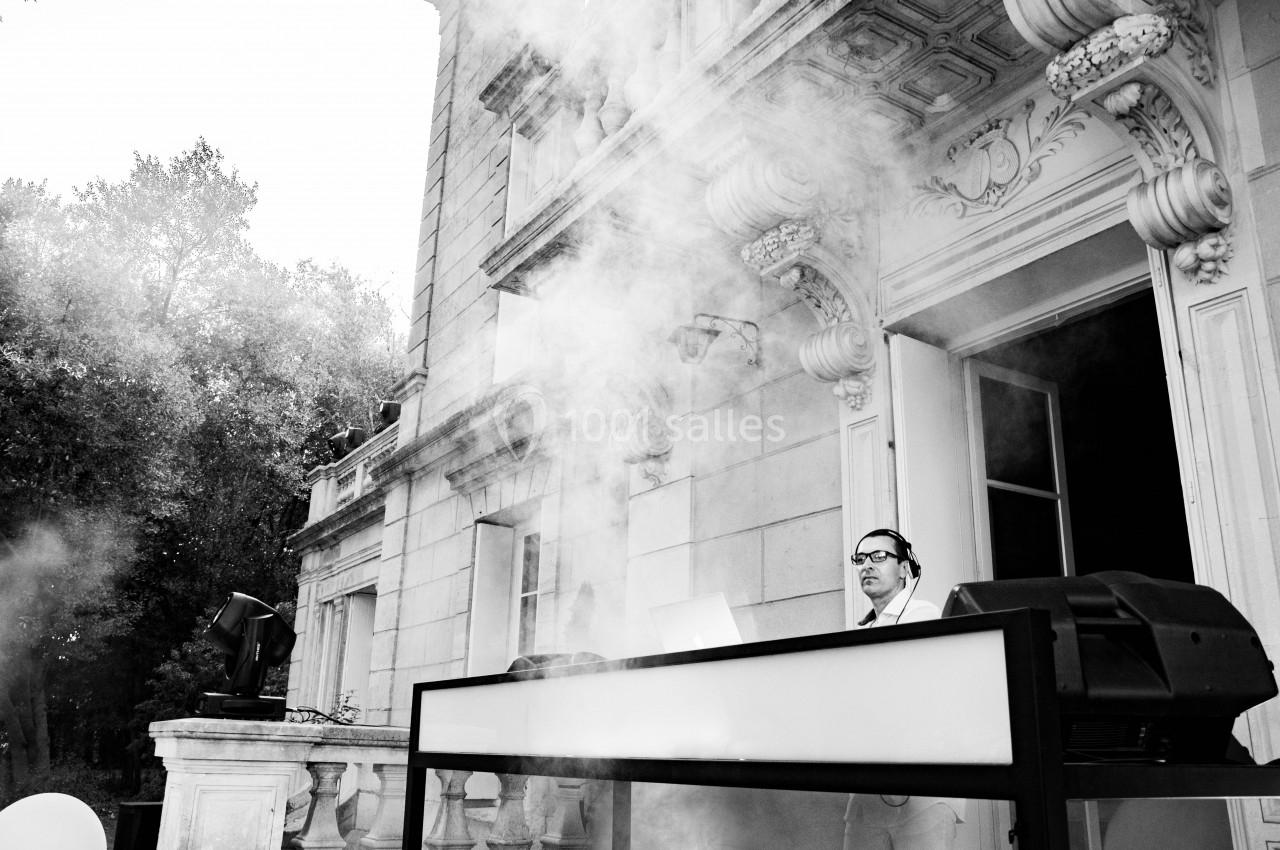 Un DJ mixe en extérieur devant un bâtiment ancien, entouré de fumée et d'équipements audio.