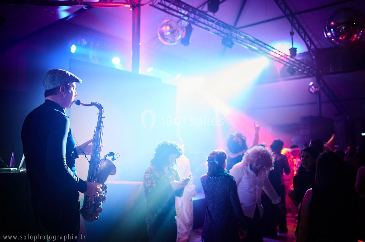 Un musicien joue du saxophone lors d'une soirée dansante avec des invités sous des lumières colorées.