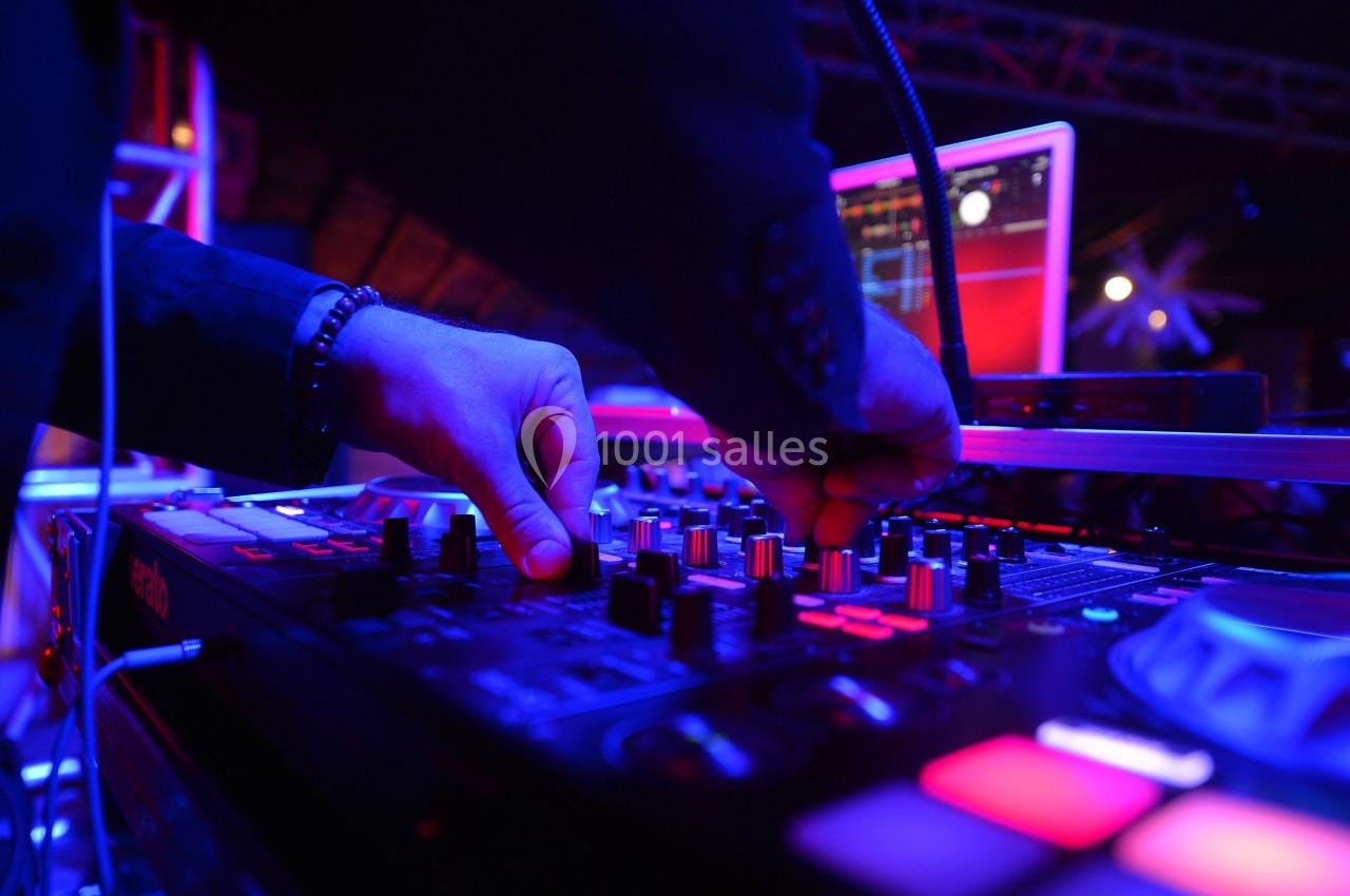 Un DJ ajuste les commandes d'une table de mixage éclairée par des lumières colorées dans un environnement sombre.