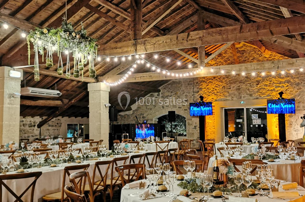 Salle de réception avec tables dressées, chaises en bois, guirlandes lumineuses et décoration végétale suspendue.