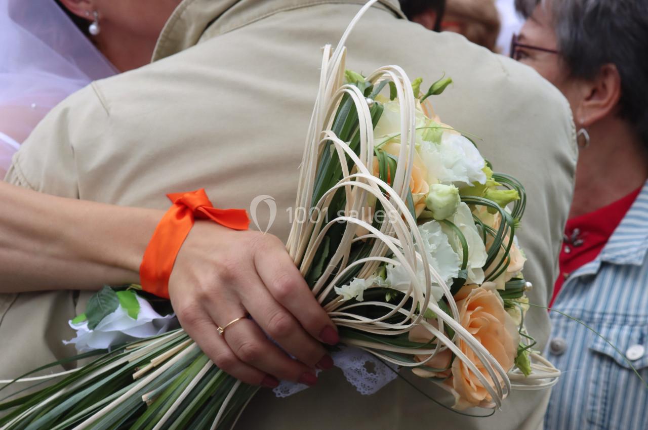 Une personne tenant un bouquet de fleurs pastel enlace quelqu'un vêtu d'un manteau beige lors d'une cérémonie.