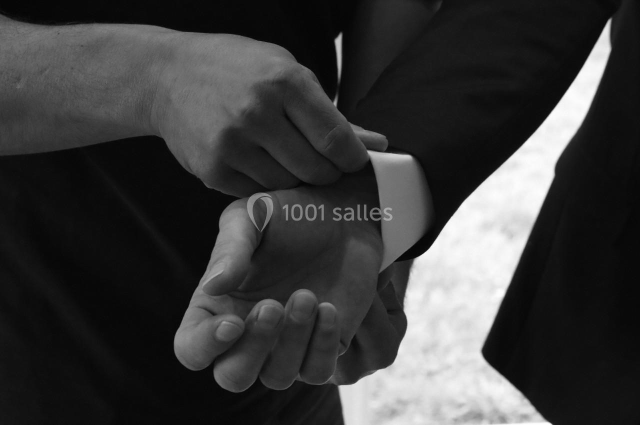 Deux mains ajustant la manche d'une chemise blanche sous une veste sombre, en lumière naturelle.