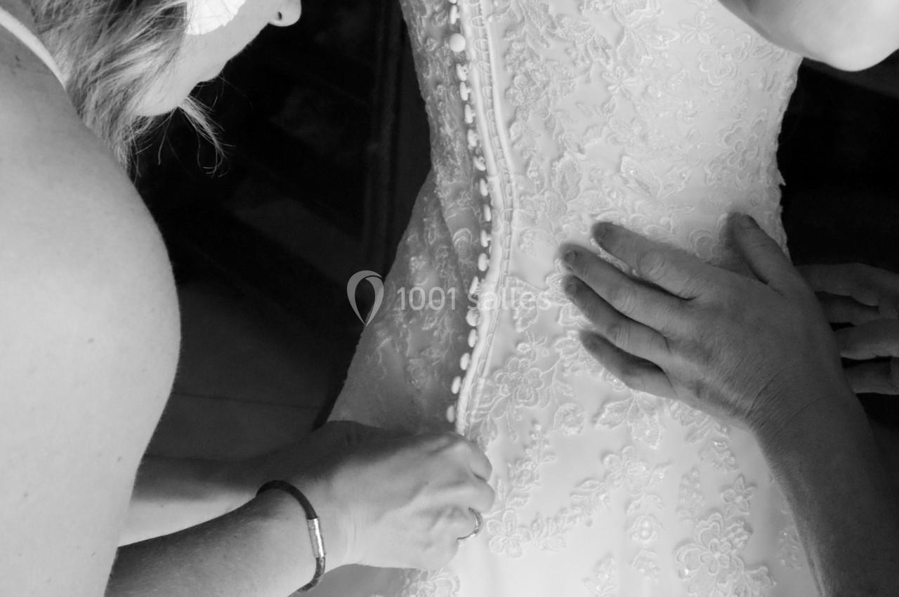 Deux personnes ajustent et boutonnent une robe de mariée ornée de dentelle.