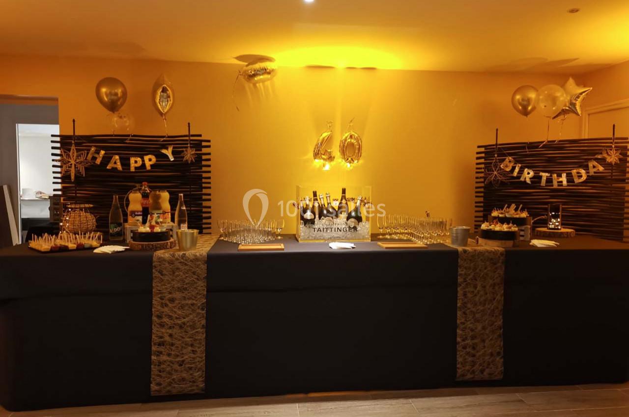 Table décorée pour un anniversaire avec ballons dorés, gâteaux, bouteilles de champagne et vaisselle.