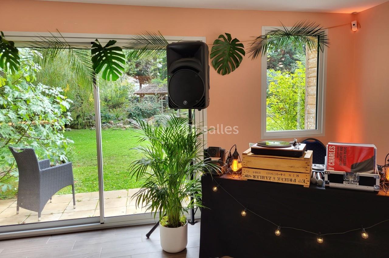 Table de mixage avec platine vinyle et enceinte dans une pièce lumineuse, vue sur un jardin verdoyant par une baie vitrée.
