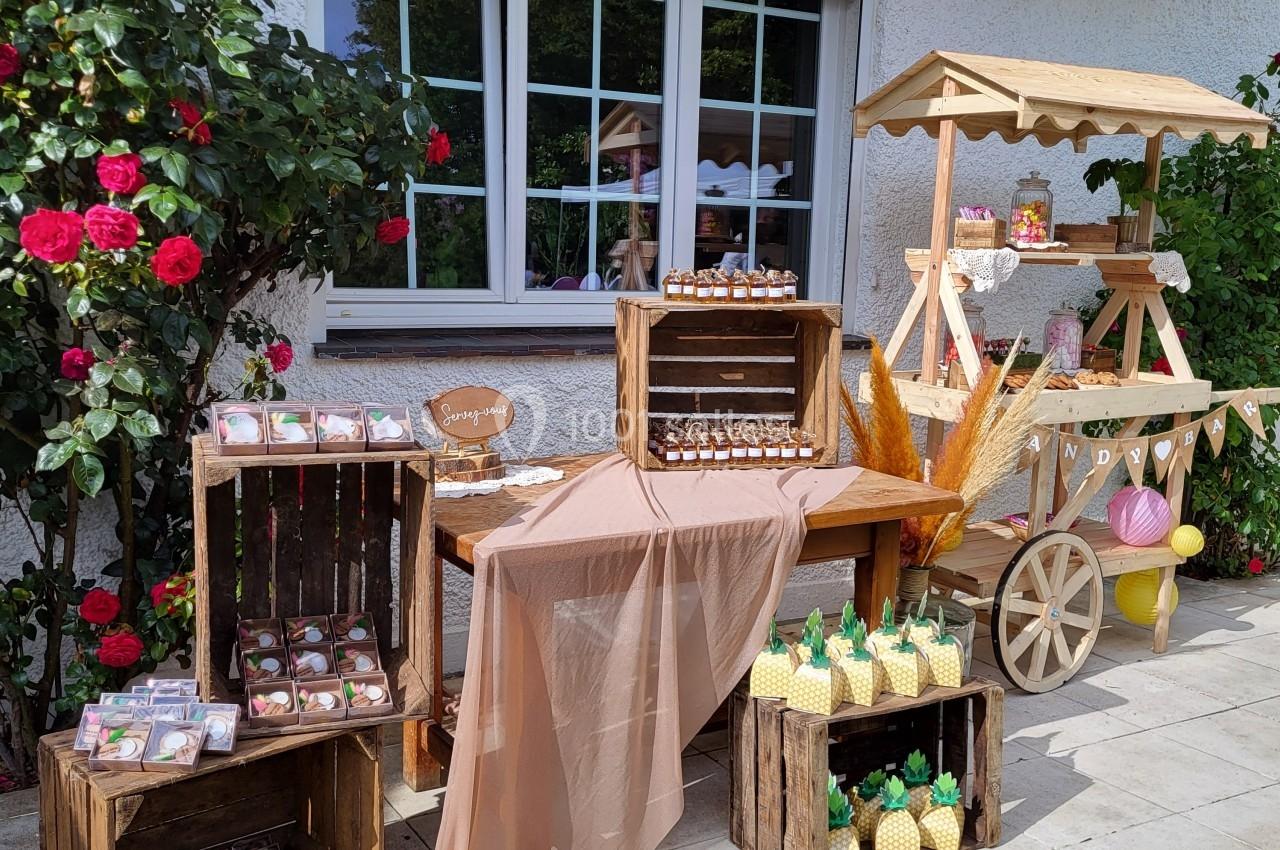Stand extérieur décoratif avec friandises, caisses en bois, nappes en tissu et fleurs près d'une fenêtre.