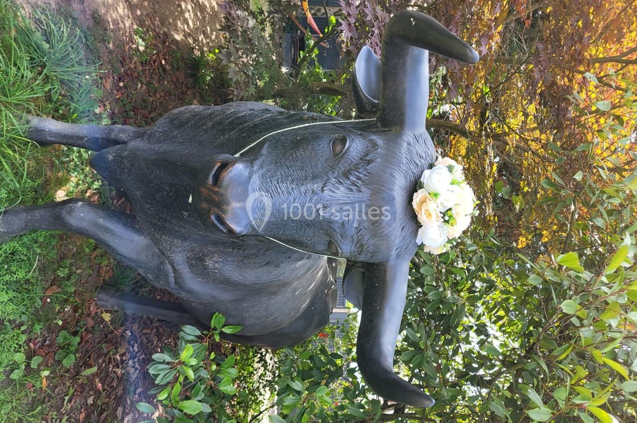 Statue de taureau ornée d'une couronne de fleurs blanches, entourée de végétation et d'arbres.