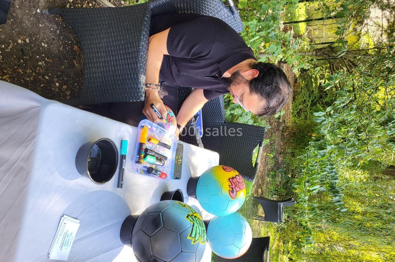 Un homme assis à une table extérieure personnalise des ballons colorés à l'aide de marqueurs.