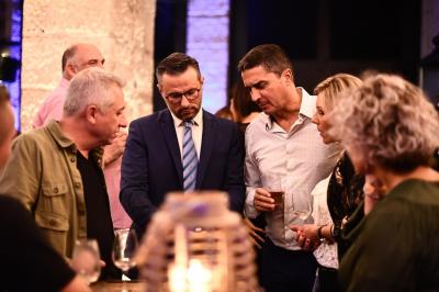 Un homme en costume montre un jeu de cartes à une jeune fille concentrée, assise à une table dans un décor en briques.