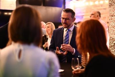 Un homme en costume montre un jeu de cartes à une jeune fille concentrée, assise à une table dans un décor en briques.