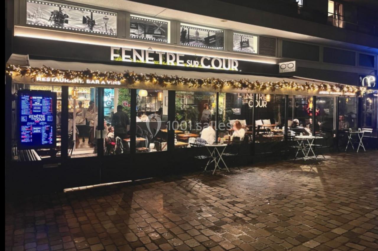 Façade d'un restaurant éclairé la nuit avec des tables en terrasse et des décorations lumineuses.