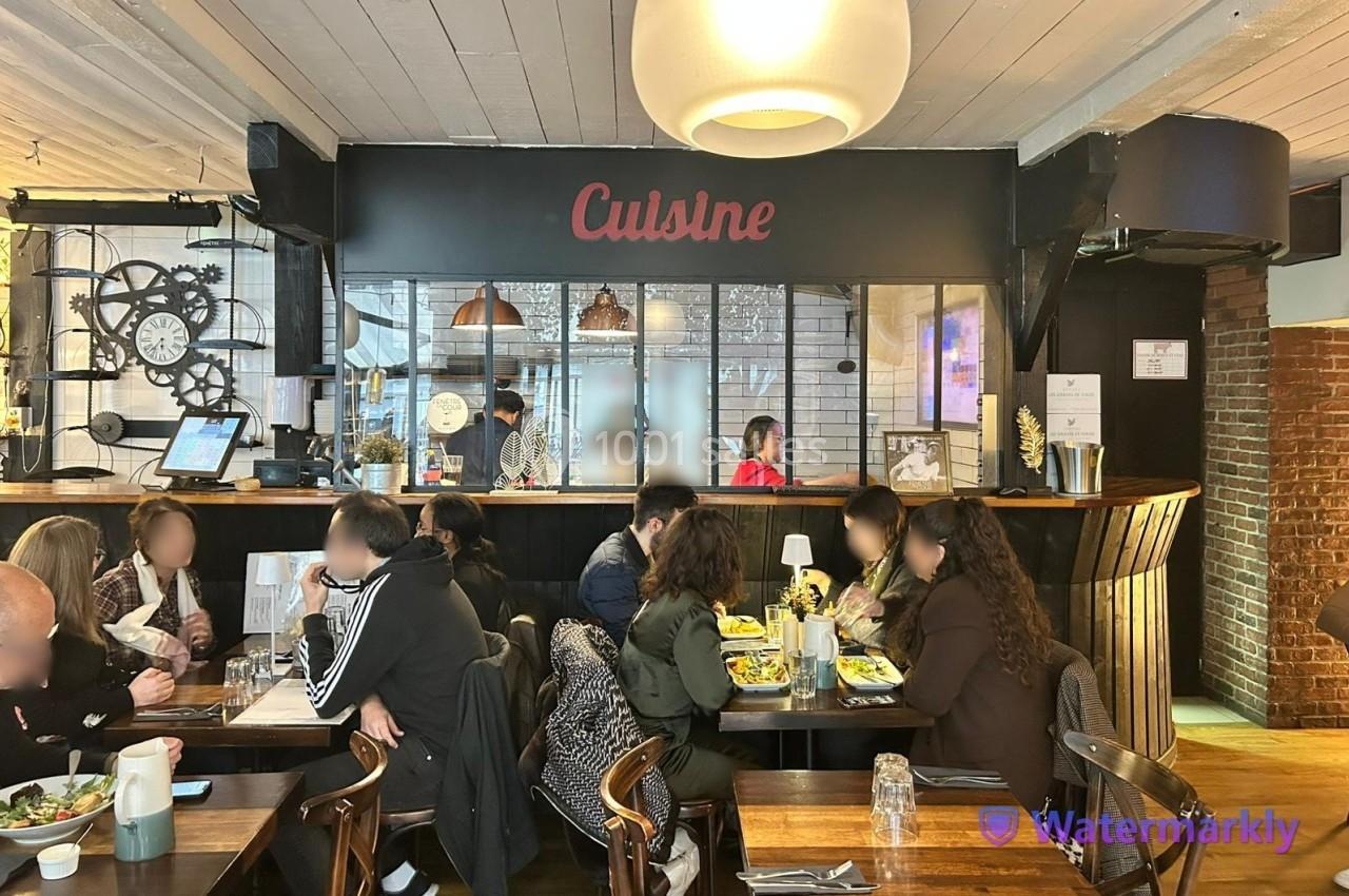 Des personnes dînent dans un restaurant à la décoration industrielle avec une cuisine ouverte en arrière-plan.