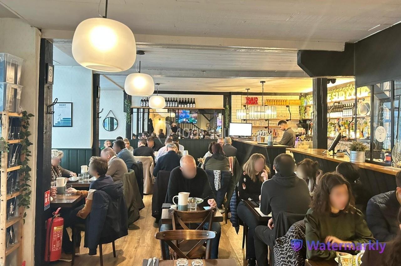 Salle de restaurant animée avec des clients attablés, un bar en arrière-plan et une décoration moderne.