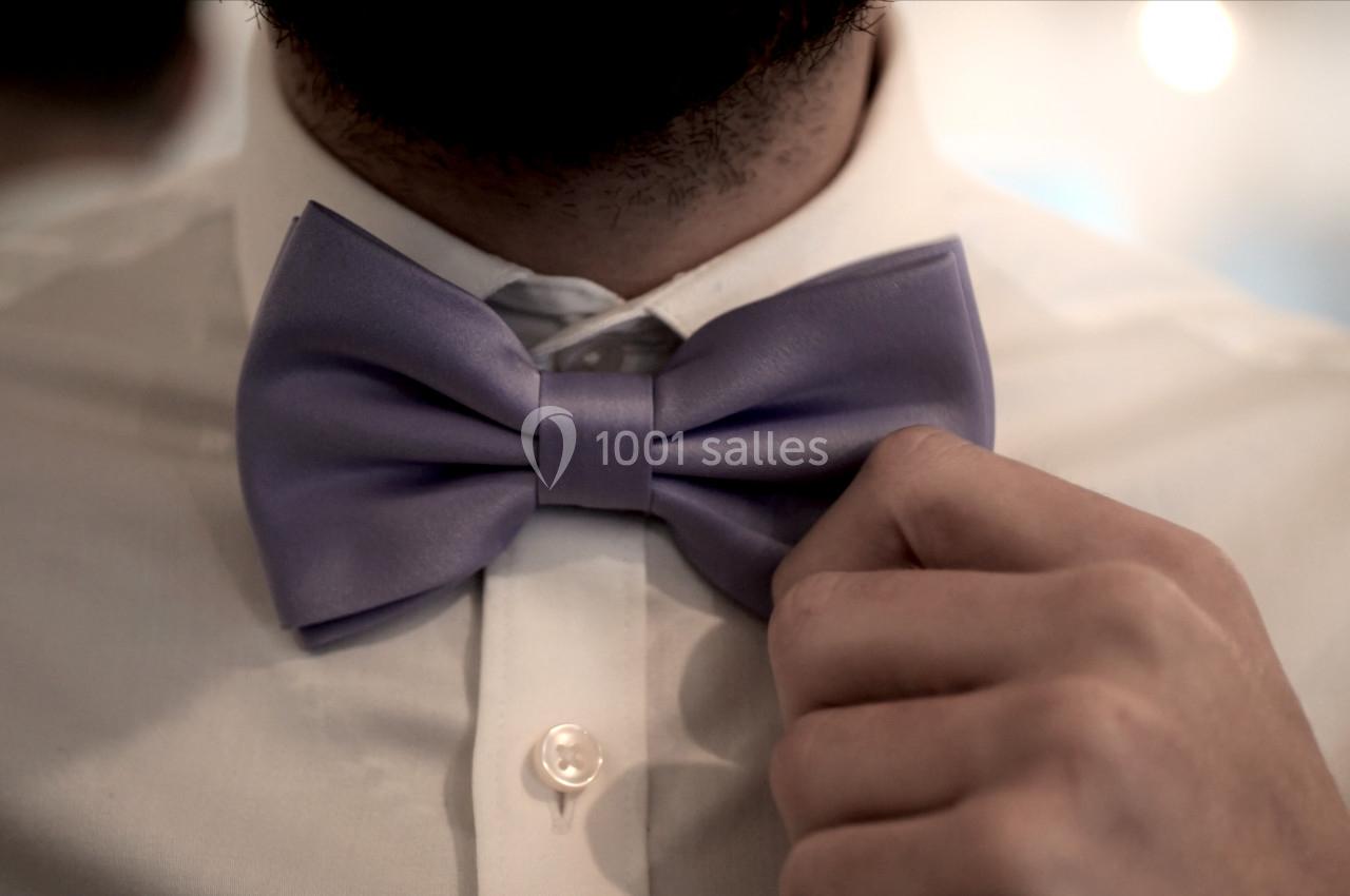Un homme ajuste un nœud papillon violet sur une chemise blanche.