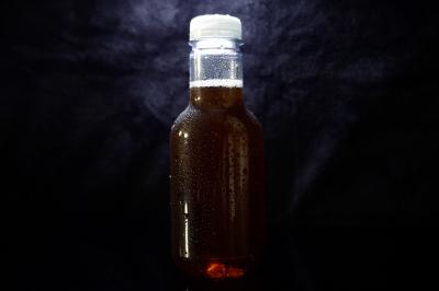 Bouteille en verre remplie de liquide brun, fermée par un bouchon blanc, sur un fond sombre.