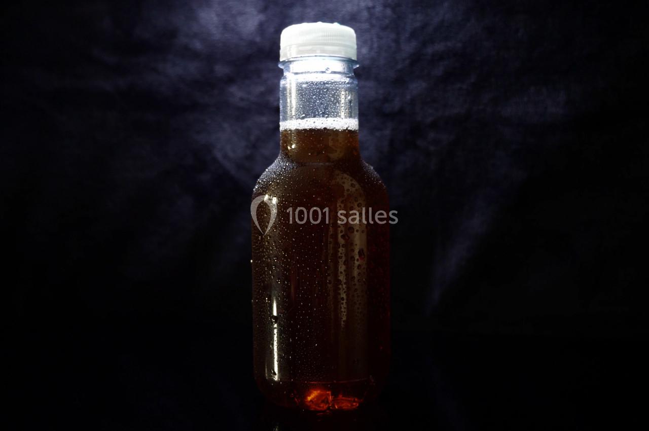 Bouteille en verre remplie de liquide brun, fermée par un bouchon blanc, sur un fond sombre.