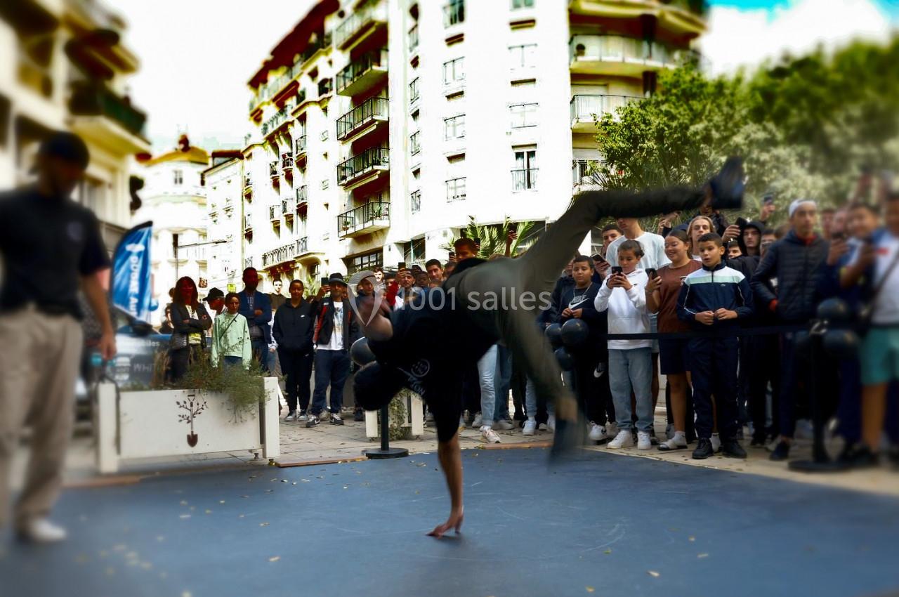 Un danseur effectue une figure acrobatique sur une main devant une foule rassemblée en extérieur.