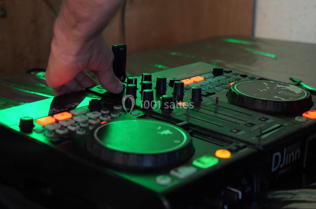 Main ajustant un bouton sur une table de mixage DJ éclairée par des lumières vertes et oranges.