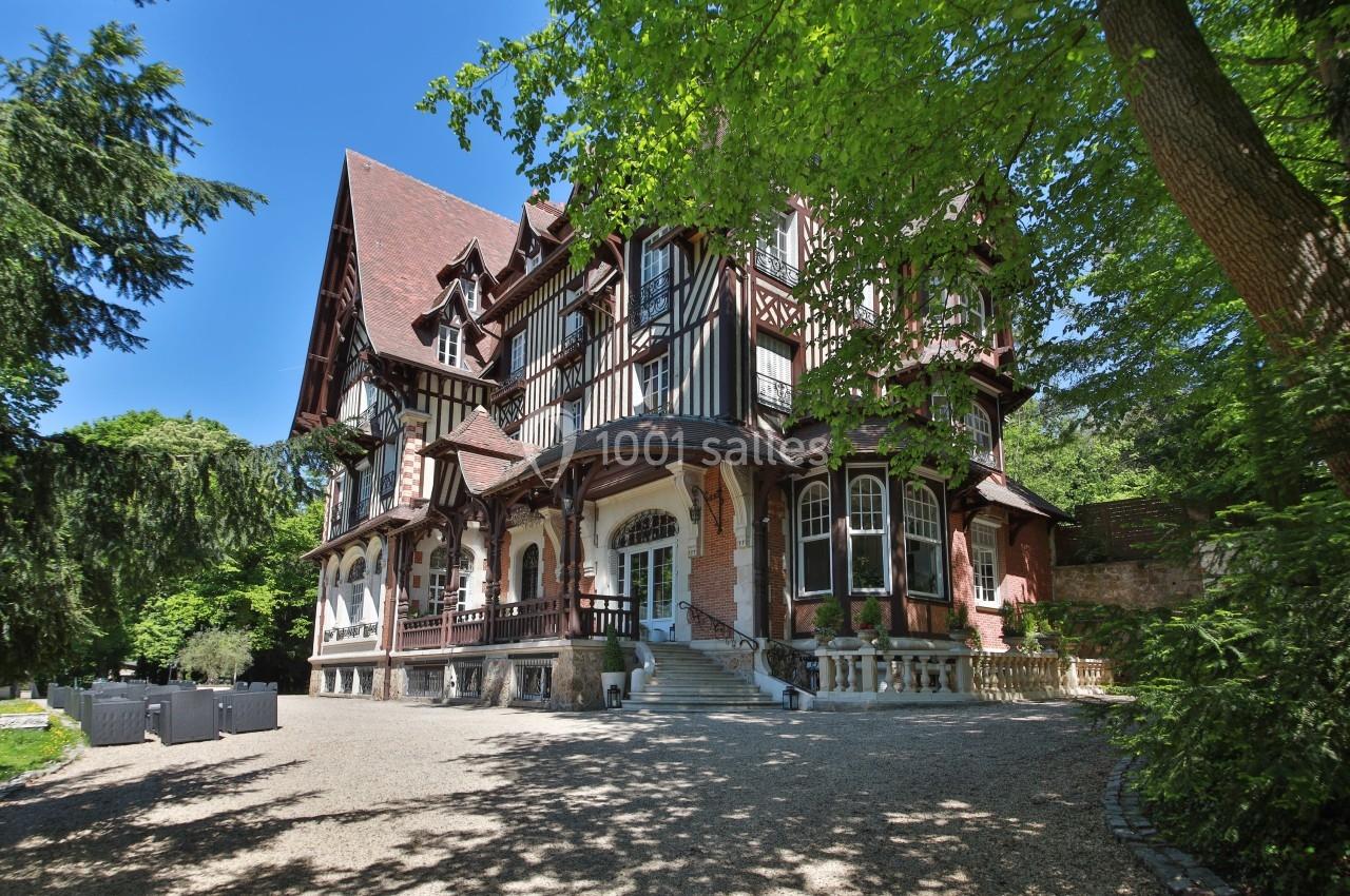Grande maison à colombages entourée d'arbres, avec une allée en gravier menant à l'entrée principale.