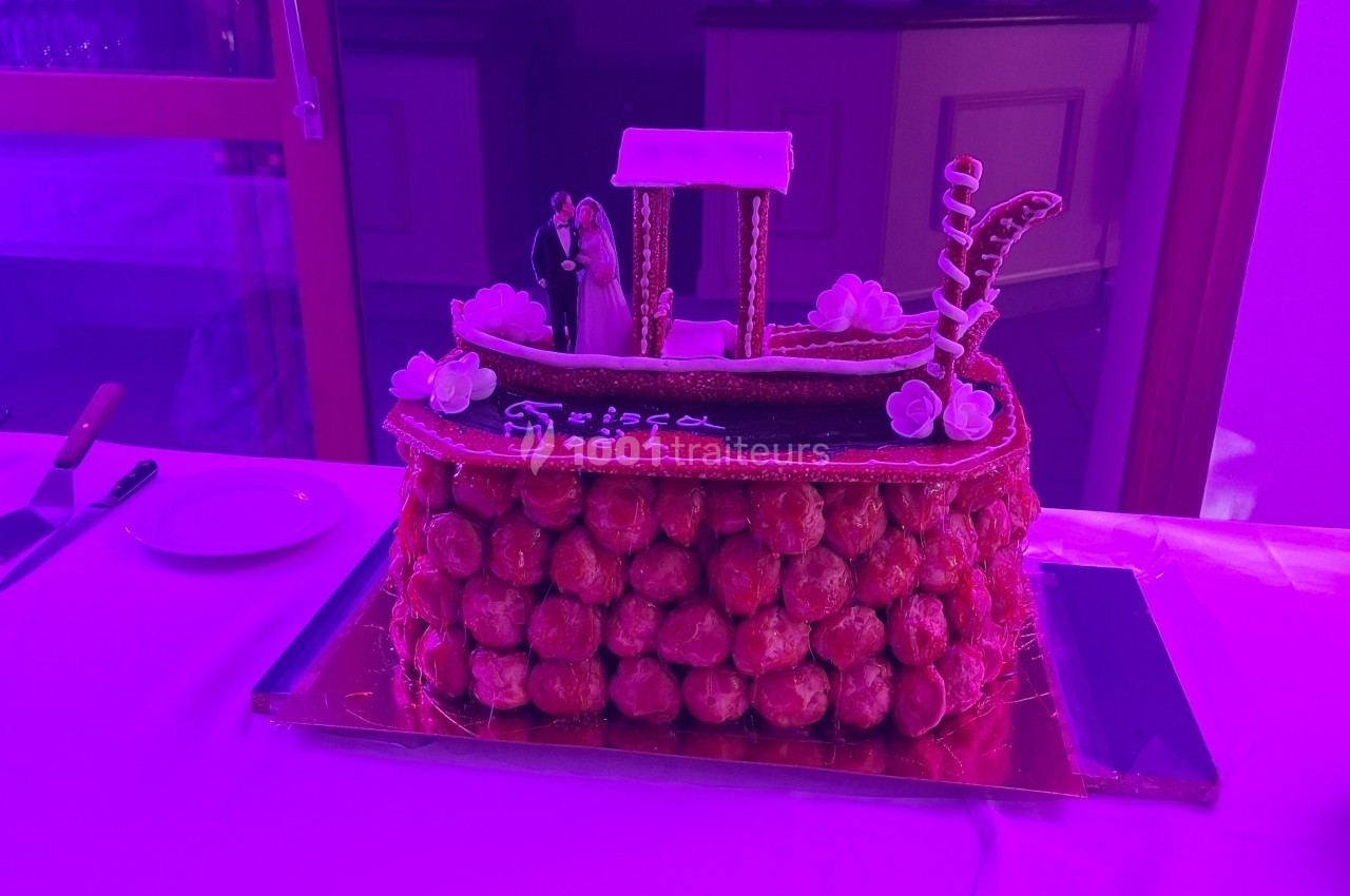 Pièce montée en choux décorée d'une gondole en sucre et de fleurs, posée sur une table éclairée par une lumière violette.