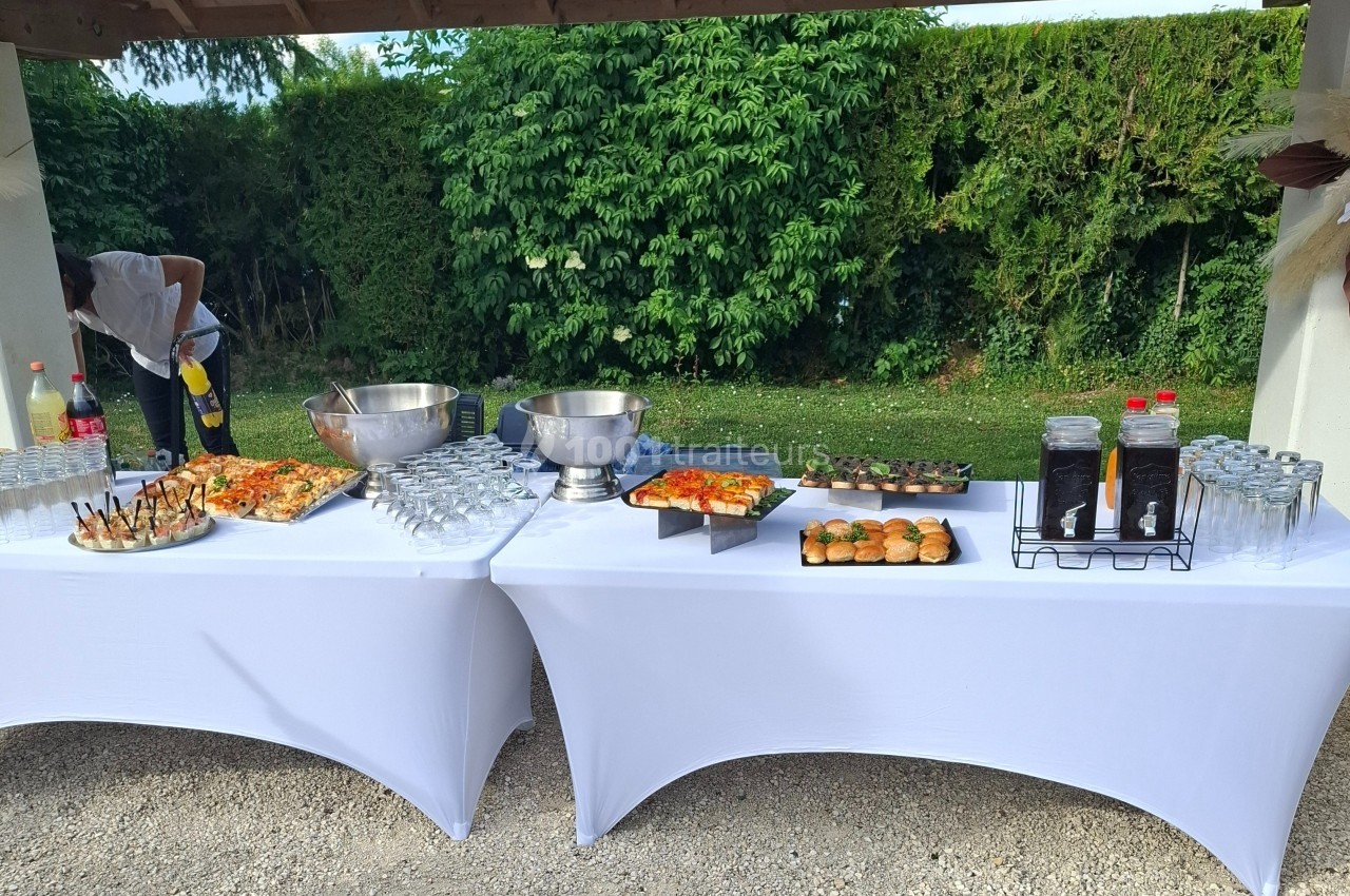 Buffet en extérieur avec tables blanches, proposant boissons, verrines, pizzas, mini-burgers et desserts.