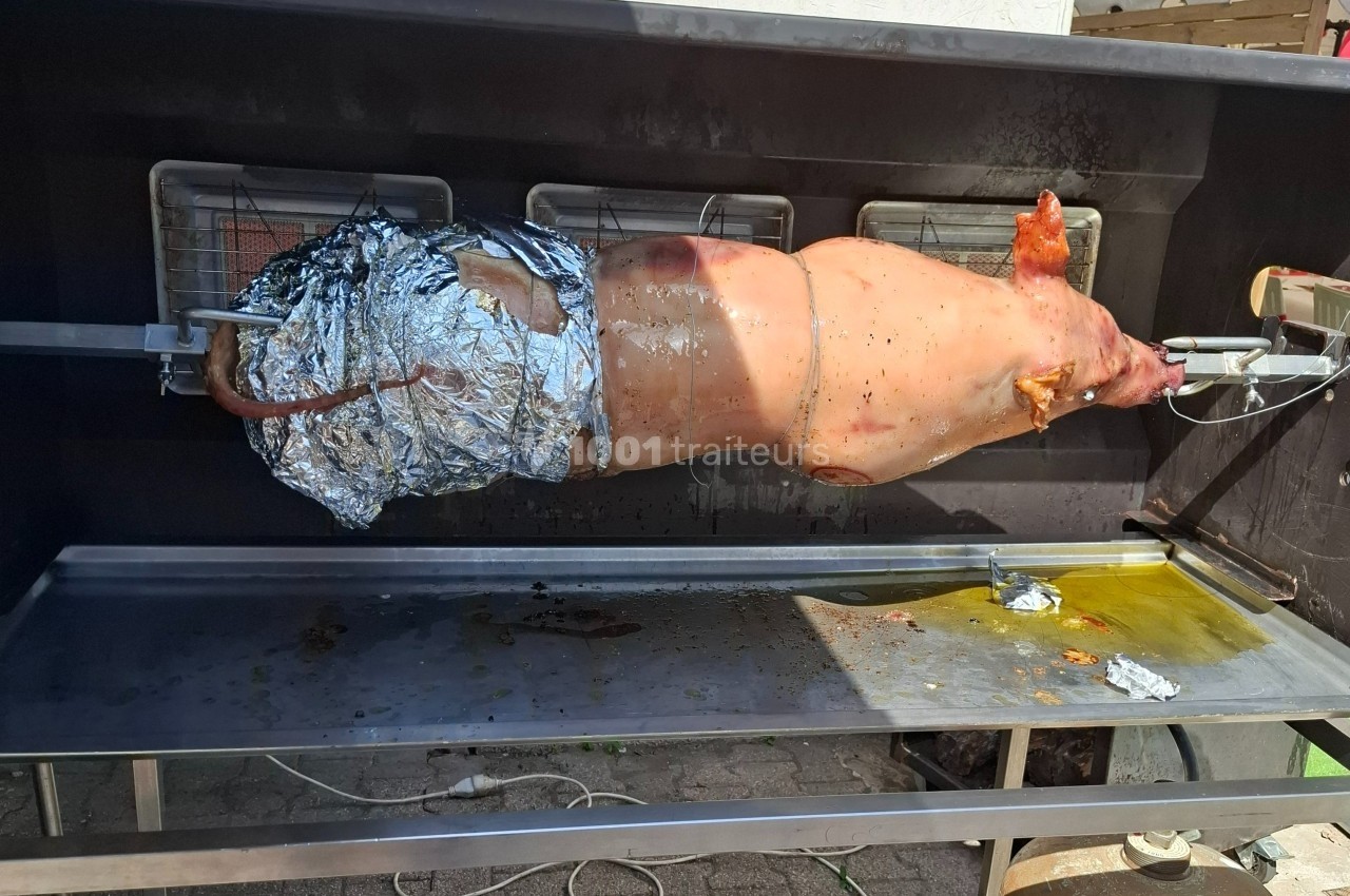 Cochon entier rôti à la broche dans un barbecue, une partie recouverte de papier aluminium.