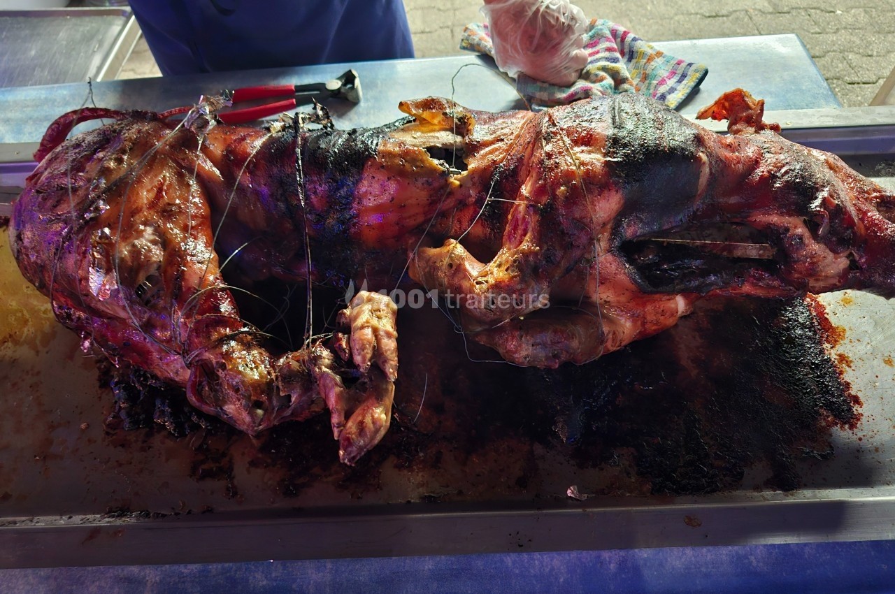 Cochon entier rôti sur une broche, posé sur un plateau métallique, avec des ustensiles en arrière-plan.