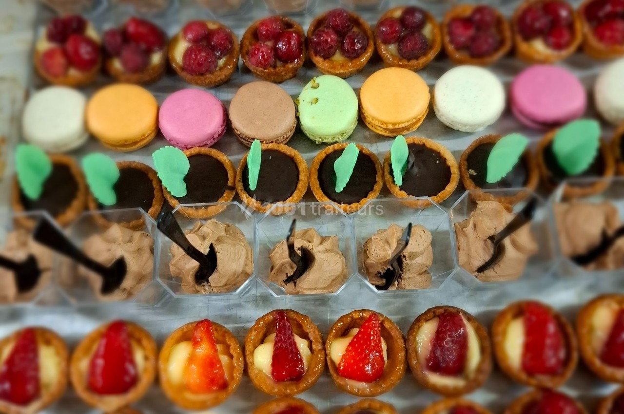 Plateau de desserts variés comprenant macarons, tartelettes aux fruits et chocolats, disposés en rangées colorées.
