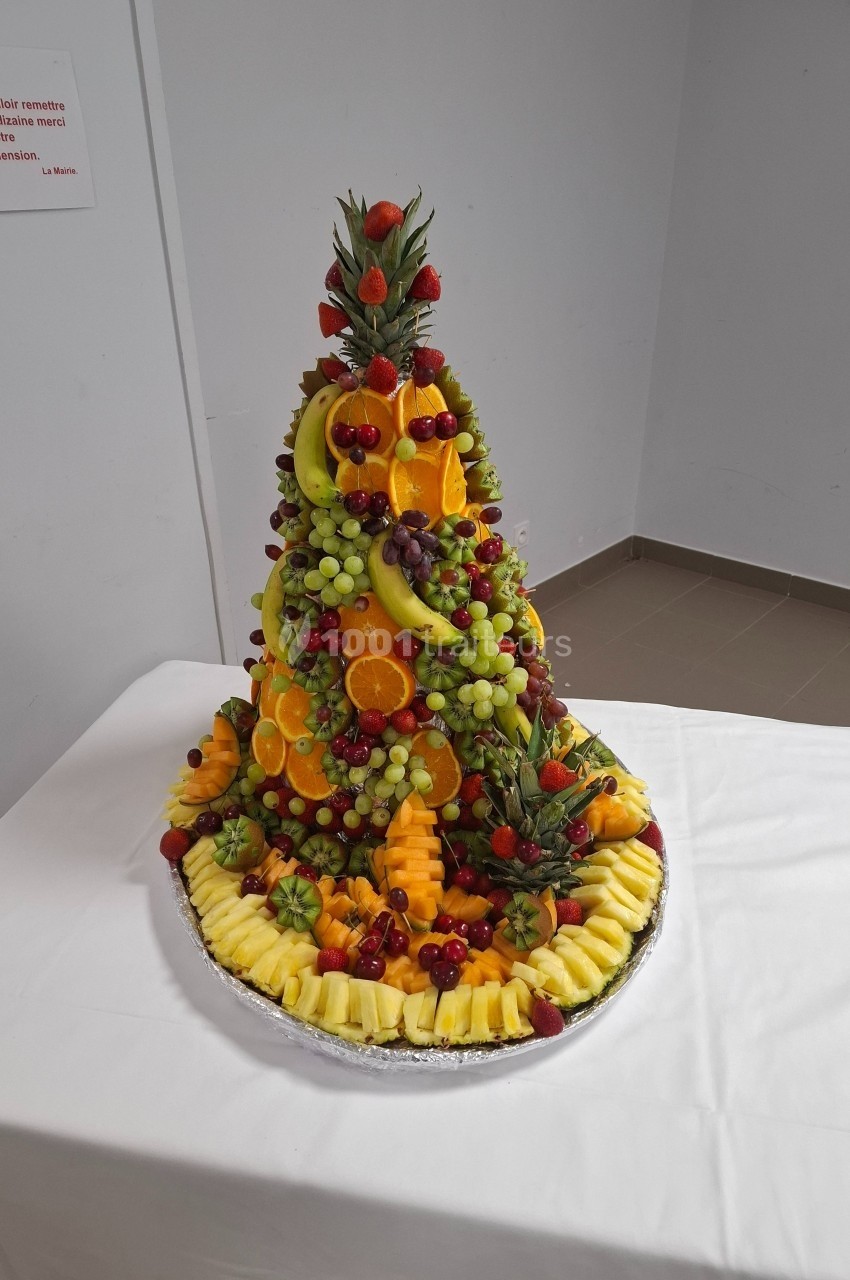 Pyramide de fruits frais variés, incluant ananas, raisins, fraises et oranges, présentée sur un plateau rond.