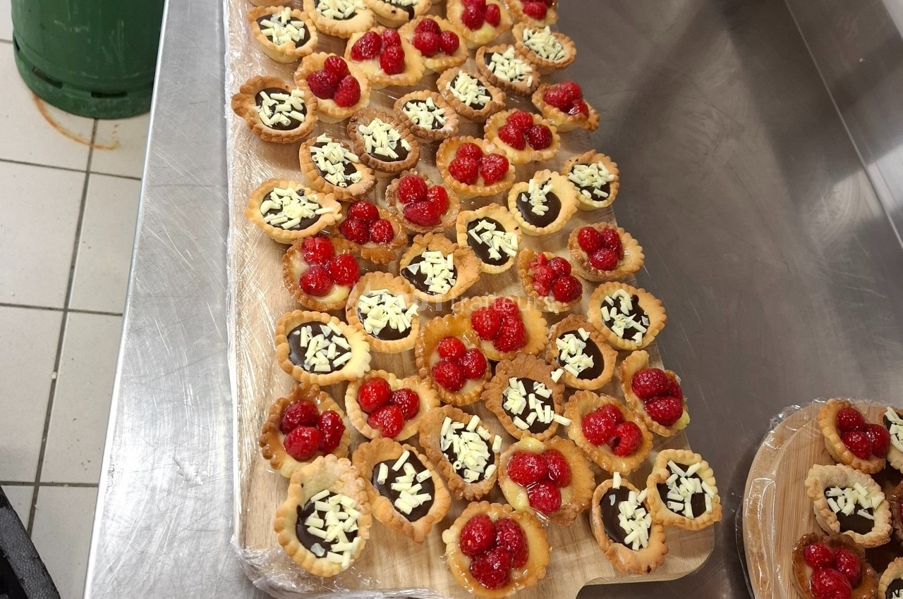 Plateau de tartelettes garnies de chocolat, éclats de chocolat blanc et framboises, disposé sur un plan de travail en…