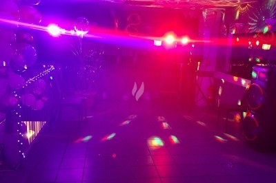 Salle décorée avec rideaux bleus, guirlandes lumineuses, vases avec fleurs et table recouverte d'une nappe blanche.